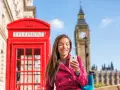 Uśmiechnięta kobieta z telefonem przed czerwoną budką telefoniczną i Big Benem. Pyta, czy w UK jest roaming, bo chce zadzwonić do domu.
