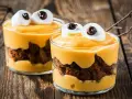 Przepis na Halloween: deser z mascarpone i ciastkiem czekoladowym, ozdobiony piankami jak oczy potwora.