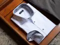 Camicia bianca piegata, con colletto e polsini a quadri marroni e neri, che mostra diversi tipi di polsini camicia.