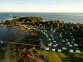 Vacker vy över Kronobergs camping med husvagnar och husbilar utspridda bland träd och vid vattnet. En brygga sträcker sig ut i det klara vattnet.