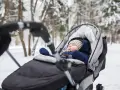 Śpiące dziecko w wózku zimą. Ciepły kombinezon, czapka i rękawiczki to podstawa, co włożyć do wózka dla noworodka zimą.