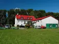 Budynek z czerwonym dachem, przypominający dawny korsarz darłówko, otoczony zielenią i samochodami.