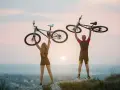 Para rowerzystów świętuje na szczycie, unosząc rowery. To idealny moment na odkrywanie najpiękniejsze odcinki z green velo.