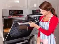 Mujer con delantal abre horno donde se hornea un pan.