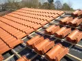Vue d'un toit en cours de pose, révélant des rangées de tuiles mécaniques en terre cuite orange vif, empilées sur des lattes de bois.