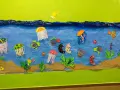 Un colorido mural de animales marinos infantiles con peces, medusas y caballitos de mar nadando en un mar azul, sobre arena.