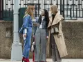 Tres mujeres conversan, una con un traje completo de **denim**, otra con chaqueta **denim** y pantalones a cuadros, y la tercera con un abrigo beige y pantalones a cuadros.