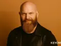 Hombre calvo con barba vikinga, mirada intensa y chaqueta de cuero.