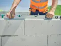 Un maçon vérifie le niveau d'une rangée de parpaings. Il se demande combien de rangée de parpaing par jour il peut poser.