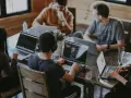 Un grupo de personas trabaja en sus portátiles en una mesa. Uno de ellos, con auriculares, parece concentrado en su pantalla, quizás buscando la clave del modelo 190.