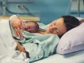 Eine Mutter hält ihr Neugeborenes im Arm, glücklich und erschöpft. Die Szene zeigt, wie lange nach Geburt im Krankenhaus die erste Bindung entsteht.