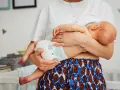 Mama tuli noworodka w pieluszce, idealnie jak ubierać noworodka latem. Lekkie ubranko i pieluszka to klucz do komfortu.