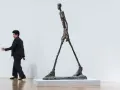 Un homme qui marche, une sculpture élancée, semble se déplacer dans un espace blanc.