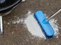 A blue brush is used to scrub a pile of white powder on a concrete patio, demonstrating how to clean concrete patio.