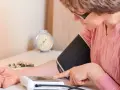 Kobieta z okularami mierzy ciśnienie, by sprawdzić objawy wysokiego ciśnienia. Na stole leżą leki.