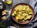 Pyszne ravioli z zielonym farszem, posypane parmezanem. Obok kawałki sera i przyprawy, gotowe do podania.