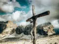 Jesus am Kreuz, eine hölzerne Figur, steht vor majestätischen Bergen unter einem dramatischen Himmel.