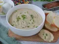 Una ciotola di cremosa salsa tonnata con maionese, guarnita con erba cipollina, accanto a pane tostato e uova sode.