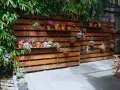 Pareti con bancali di legno ospitano piante grasse e fiori, creando un angolo verde.