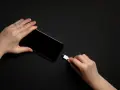 Dwie dłonie trzymają smartfon i biały kabel USB-C. Zastanawiasz się, do ilu procent ładować telefon, by zadbać o jego baterię?