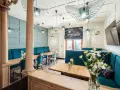 Wnętrze restauracji z turkusowymi kanapami, drewnianymi stołami i ozdobnymi lampami.