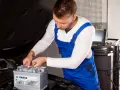 Mechanik w niebieskim kombinezonie wykonuje kodowanie akumulatora Varta w samochodzie.