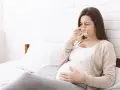 Kobieta w ciąży z chusteczką przy nosie, czuje się niedobrze.