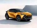 Nowy, złoty Toyota C-HR Hybrid z czarnym dachem prezentuje się dynamicznie na tle minimalistycznej architektury.