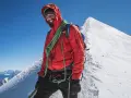 Uśmiechnięty alpinista na szczycie Mont Blanc, w czerwonej kurtce i z liną, gotowy na dalszą wspinaczkę.