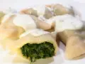 Pierogi ze szpinakiem polane sosem śmietanowym na białym talerzu.