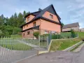 Urocze **mogielica schronisko** w otoczeniu zieleni. Jasnoróżowy budynek z czarnym dachem, obok drewniana stodoła.