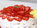 En vacker vegansk jordgubbstårta täckt med färska jordgubbar och fluffig grädde. Perfekt för sommaren!