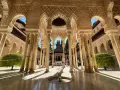 Intricate arches and columns of the Alhambra, a perfect postcard from Granada. Sunlight streams through, illuminating the detailed stonework.