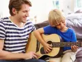 Ojciec uczy syna grać na gitarze. Radosna szkoła gry na gitarze w domowym zaciszu.