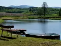 Idealne miejsce na camping nad stawami: łódka przy pomoście, ławka i spokojna tafla wody.