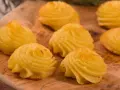 Patate duchessa dorate e invitanti, disposte su un tagliere di legno, pronte per essere gustate.