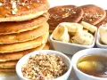 Pile de pancakes dorés arrosés de miel, accompagnés de rondelles de banane, de noix concassées et d'une cuillère de miel. Un délice pour le petit-déjeuner !