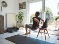 Un homme fait des dips sur une chaise, une idée de quel sport faire à la maison. Un tapis de yoga est au sol.