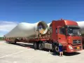 Pomarańczowy samochód ciężarowy przewozi ogromne łopaty turbin wiatrowych.