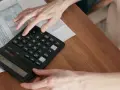 Manos calculando el total de suplidos en un formulario fiscal.