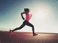 Donna corre su strada asfaltata al tramonto, con il sole che illumina la scena. Questo è un esempio di tempo run, un allenamento per migliorare la velocità.