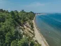 Mechelinki klif porośnięty drzewami, z piaszczystą plażą i turkusowym morzem. W oddali widać zabudowania i falochron.