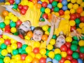 Drei Kinder in gelben T-Shirts spielen in einem Bällebad. Perfekte Ausflugsziele mit Kindern für Spaß und Lachen.