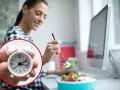 Mujer comiendo ensalada en su escritorio, con un reloj que marca el tiempo para comer en el trabajo.