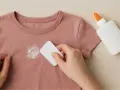 Mano raspando un parche de pegamento seco de una camiseta rosa. Un consejo para como quitar parches de la ropa.