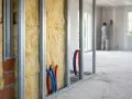Isolation et tuyauterie dans une structure métallique. Un ouvrier travaille au plâtre en arrière-plan. Une entreprise de second oeuvre en pleine action.