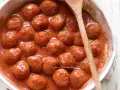 Polpette al sugo fumanti in una ciotola, pronte per essere gustate. Un cucchiaio di legno le accompagna.