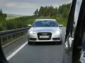 Silberner Audi auf der Autobahn, blendet mit Lichthupe. Vorbei an grünen Wäldern und einer Leitplanke.