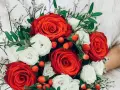 Un ramo de rosas rojas y blancas, adornado con bayas rojas y delicadas flores blancas, evoca la belleza de las flores de febrero.