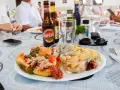 Malta jedzenie: talerz pełen smakołyków z tuńczykiem, fasolą i oliwkami, obok piwo i ludzie przy stole.